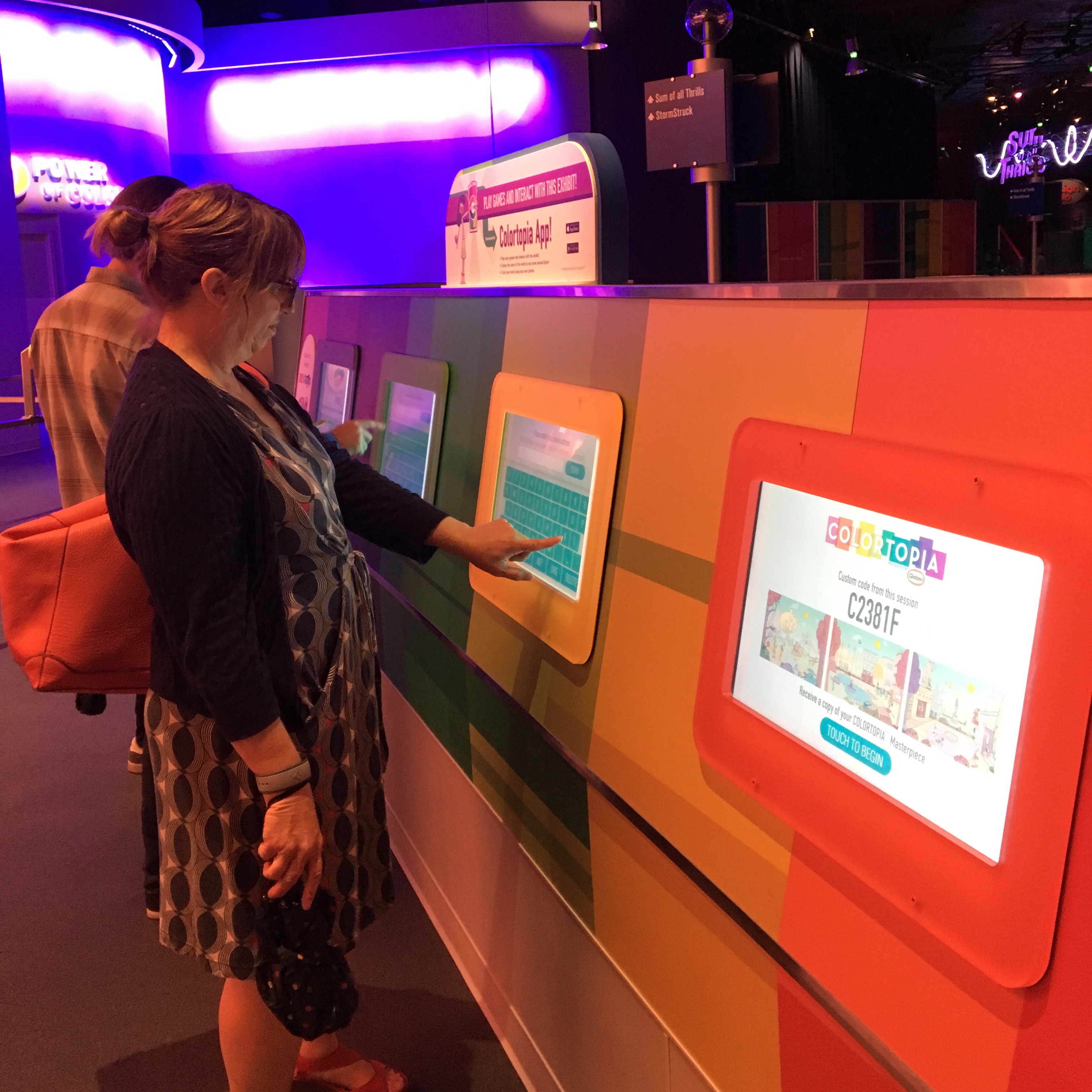 A crowd of people on their mobile phones, looking at a large screen display on the wall.